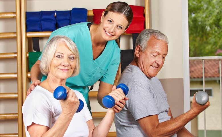Senior couple lifting dumbbells with Physiotherapist helping behind